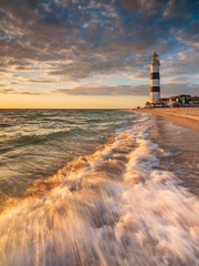 Wall Mural - wide angle view through sea wave to old lighthouse at sunset time with copy space