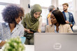 © Santi Nunez/Stocksy - muslim woman in hijab, a african woman and curly hair man working together in the office using laptop.