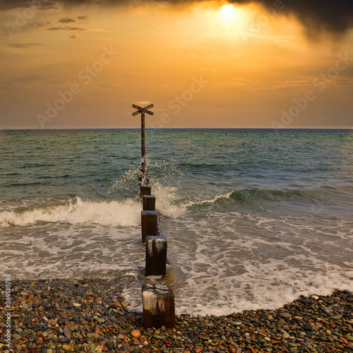 Fotografía Wooden pillars and metal cross on Findhorn Beach, Moray Coast, Scotland with dramatic sunrise
