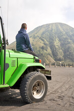 Man Visiting Bromo Volcano By Jeep And Sitting On The Hood Of The Car