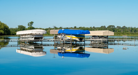 Docked boats on lifts are reflected in the calm water of a pretty lake in Minnesota, on a sunny summer day with beautiful clear blue sky.