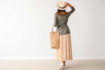 Beautiful young woman with wicker bag near light wall