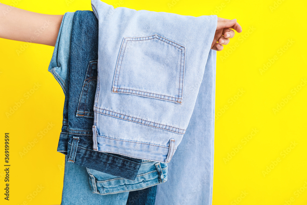 Female hand with stylish jeans pants on color background