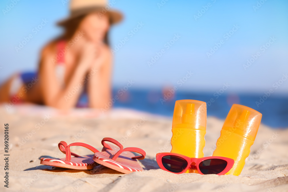 Sunscreen cream, sunglasses and flip-flops on beach sand