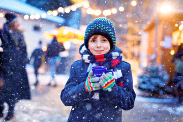 Wall Mural - Little cute kid boy drinking hot children punch or chocolate on German Christmas market. Happy child on traditional family market in Germany, Laughing boy in colorful winter clothes