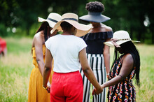 Group Of Four Gorgeous African American Womans Wear Summer Hat Holding Hands And Praying At Green Grass In Park.