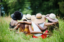 Back View  Of Group Four Gorgeous African American Womans Wear Summer Hat Sitting At Green Grass In Park.