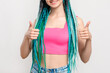© golubovy - Z generation woman with blue hair braids. Like gesture. Satisfied lady in pink crop top with dyed dreads showing thumbs up isolated on white. Creative ethnic hairstyle. Beauty salon. Perfect choice.