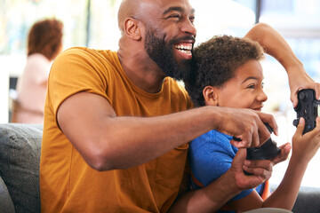 African American Father And Son Sitting On Sofa At Home Playing Video Game Together