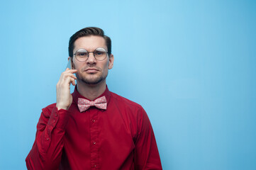 Wall Mural - Portrait of a handsome young man in a red shirt and glasses with a smartphone