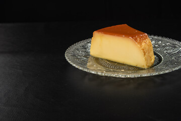 Milk pudding on a plate on black table with black background, selective focus