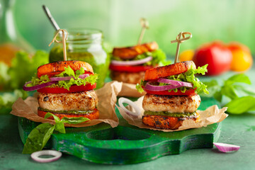 Sticker - Delicious roasted pumpkin turkey burger with tomatoes and pesto on green wooden board.