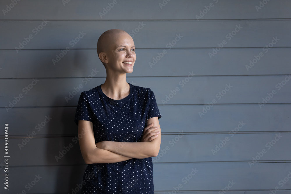 Happy young sick hairless woman with oncology isolated on wooden background look in distance dreaming, smiling ill bald female patient struggling with cancer, feel hopeful optimistic of recovery - obrazy, fototapety, plakaty 
