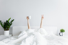 Good Morning Concept - Female Hands With Coffee Cup And Victory Sign Sticking Out From The Blanket At Home Or Hotel