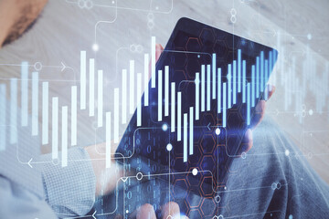 Double exposure of man's hands holding and using a digital device and forex graph drawing. Financial market concept.