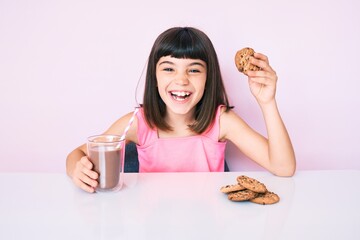 Wall Mural - Young little girl with bang sitting on the table having breakfast smiling and laughing hard out loud because funny crazy joke.