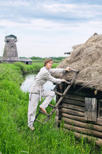 Village Young Man In White Linen Clothes Climbs Up A Ladder To The Thatched Roof Of A Small Hut
