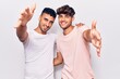 © Krakenimages.com - Young gay couple wearing casual clothes looking at the camera smiling with open arms for hug. cheerful expression embracing happiness.
