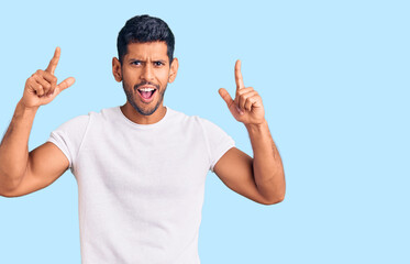 Young latin man wearing casual clothes smiling amazed and surprised and pointing up with fingers and raised arms.