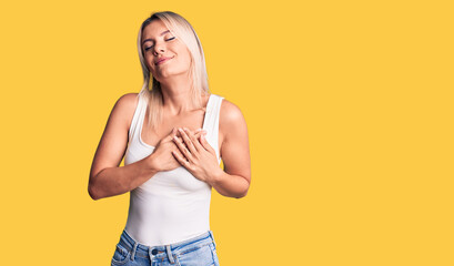 Young beautiful blonde woman wearing casual sleeveless t-shirt smiling with hands on chest with closed eyes and grateful gesture on face. health concept.