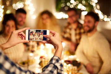 Poster - holidays, celebration and people concept - happy friends taking picture with smartphone at home christmas dinner party