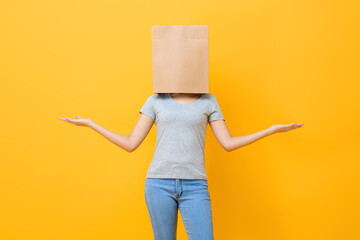 Anonymous woman in casual attire cover head with paper bag doing open hand gesture in yellow studio background