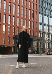 Full length portrait of a fashionable girl outdoors on the background of modern architecture, looking and posing at camera.Lifestyle stylish lady on the background of a building standing on the street