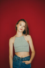 Attractive model in jeans and light t-shirt isolated on red background, posing at camera, looking intently. Sexy girl stands on red wall background. Vertical photo.