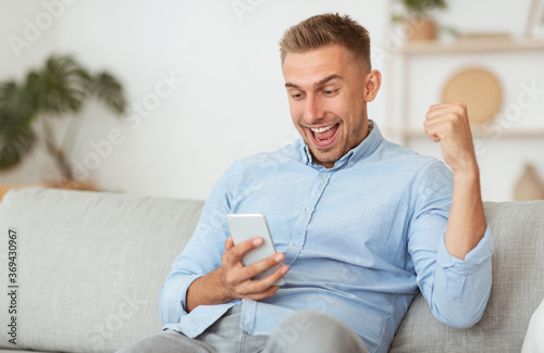 Photographie Excited male employee feeling ecstatic holding phone