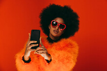Young Woman Taking Selfie On Phone While Wearing Sunglasses Against Orange Background