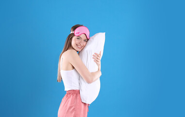 Wall Mural - Young woman with pillow and sleep mask on blue background