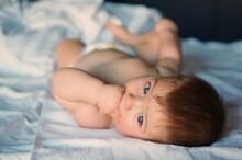 Portrait Of Cute Baby With Blue Eyes Lying On Bed At Home