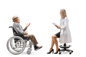 Canvas Print - Young female doctor sitting on a chair and talking to an elderly male patient in a wheelchair