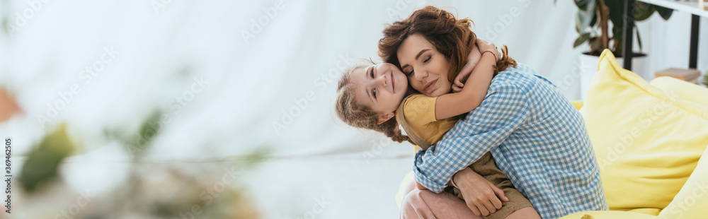 horizontal image of happy nanny hugging smiling kid while sitting on sofa - obrazy, fototapety, plakaty 