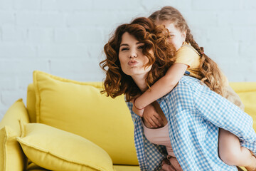 Wall Mural - young nanny making duck face while piggybacking kid at home