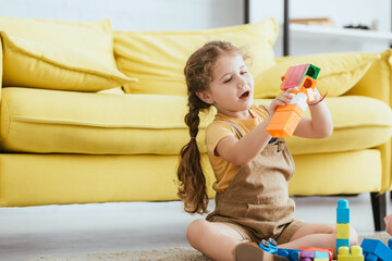 Wall Mural - cute kid playing with building blocks while sitting on floor near yellow sofa