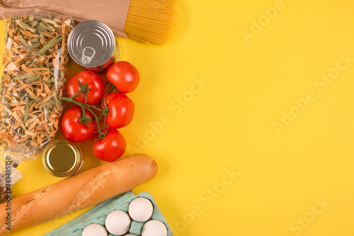 Top view on food donations on green background with copyspace - pasta, fresh vegatables, canned food, baguette, eggs, organic oil. Donation and contactless delivery food concept