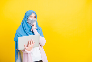 Wall Mural - Asian Muslim Arab, Portrait of happy beautiful young woman Islam religious wear veil hijab and face mask protect she quarantines disease coronavirus hold laptop computer and thinking question