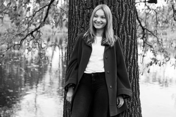 Black and white portrait of a pensive girl in an autumn park next to an old oak tree by the lake