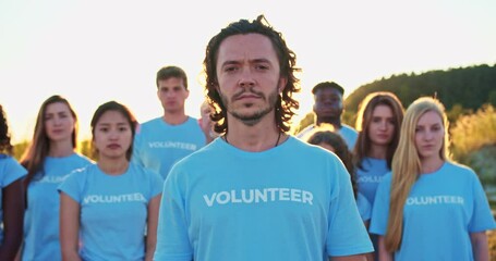 Wall Mural - Portrait of Han with group of eco activists in background. Pretty Caucasian female volunteer looking at camera and saying: I Am Volunteer. Volunteering, environmental conservation.