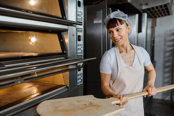 Wall Mural - portrait of a woman baker holding a wood peel in a bakery.