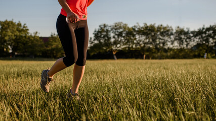 Close up of a woman's legs making sport, she is running on a grass in the midst of nature on sunset.