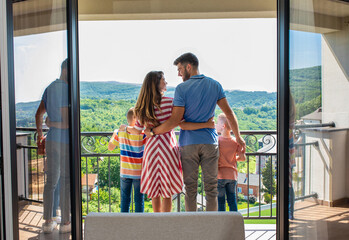 Wall Mural - rear view of smiling family of four in the hotel room standing at terrace embracing each other.