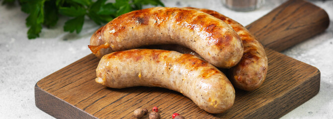 Grilled sausages on a wooden serving Board on a light gray kitchen table. Fried sausages on a serving Board. Banner