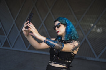 Sticker - Cool young lady with blue hair, tattoos, and sunglasses, wearing a crop top taking a selfie