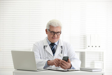 Wall Mural - Senior doctor with smartphone at table in office