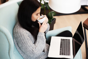 Young woman working on laptop computer while sitting at the living room