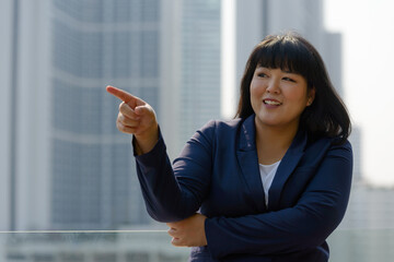 Happy young beautiful overweight Asian businesswoman against view of the city