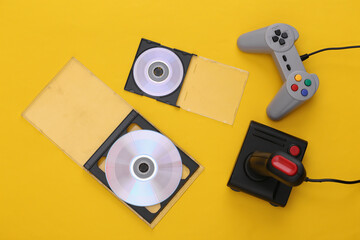 Wall Mural - Retro gamepad and joystick, CD's on blue yellow background. Gaming, video game competition. Top view