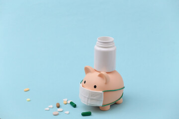 Wall Mural - Piggy bank in medical mask with pills bottle on blue background. Financial crisis. Covid-19 pandemic